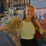 Chloe Moffat holding a bouquet of flowers in a street