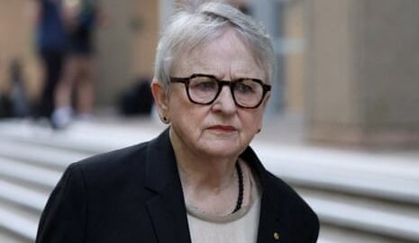 Commissioner Virginia Bell, wearing glasses and a dark blazer, walks near outdoor steps