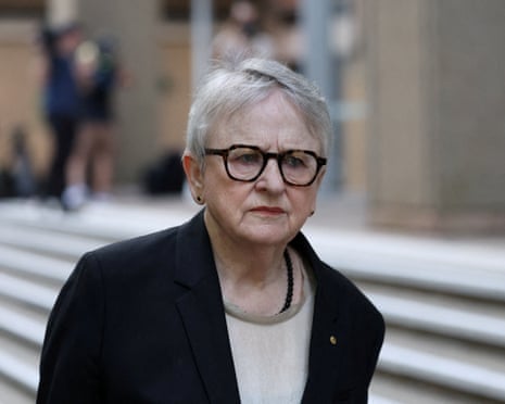 Commissioner Virginia Bell, wearing glasses and a dark blazer, walks near outdoor steps