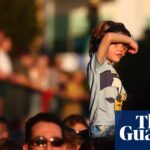 A boy sits on someone's shoulders shielding his eyes, above a crowd watching Riverfire