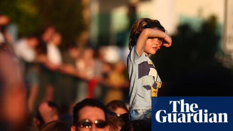A boy sits on someone's shoulders shielding his eyes, above a crowd watching Riverfire