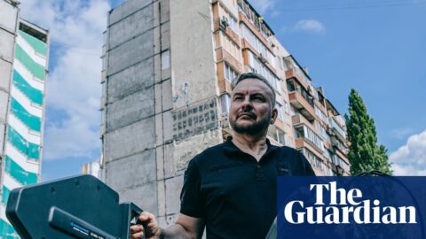 Serhii Beskrestnov holds a spectrum analyser near damaged apartment buildings in Kyiv