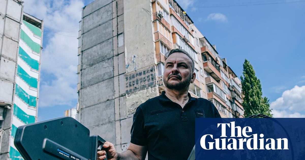 Serhii Beskrestnov holds a spectrum analyser near damaged apartment buildings in Kyiv
