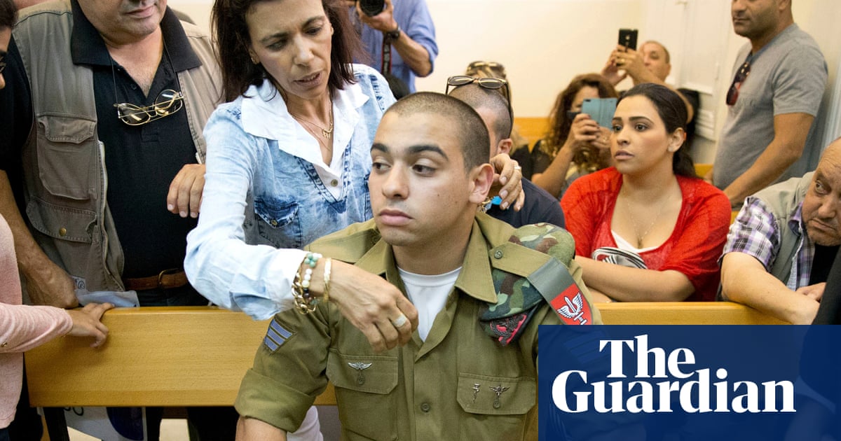 A man in military uniform sits on a wooden bench in a courtroom and is comforted by a woman.