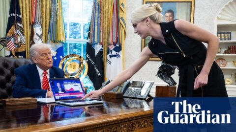 Donald Trump looks on as Natalie Harp, an aide, places a computer displaying a news report about the stock market, on his desk.