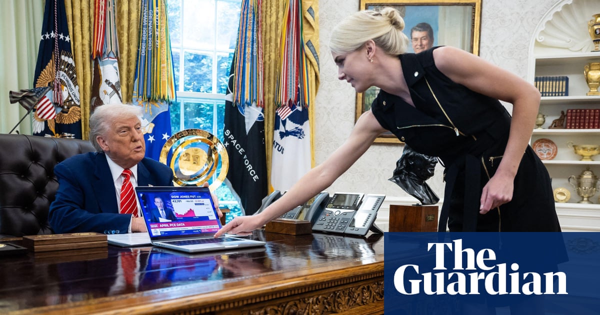 Donald Trump looks on as Natalie Harp, an aide, places a computer displaying a news report about the stock market, on his desk.