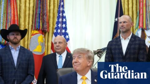 Man sits at desk and smiles as people stand behind him