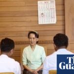 Aung San Suu Kyi sits at a wooden table talking with two officials