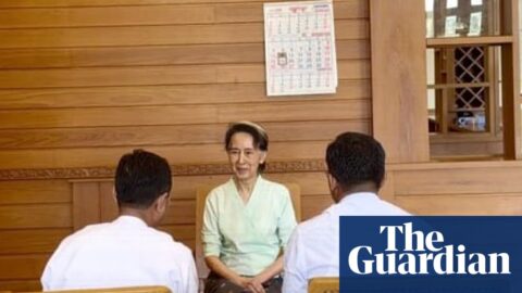 Aung San Suu Kyi sits at a wooden table talking with two officials