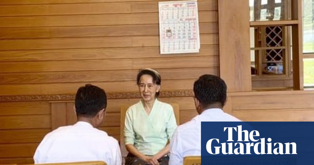 Aung San Suu Kyi sits at a wooden table talking with two officials
