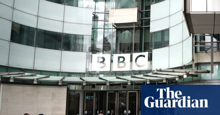 The curved frontage of BBC Broadcasting House in Portland Place, London, with the BBC logo on large glass windows above the doors. People with cameras stand in the courtyard in the foreground with others talking and going towards the doors.