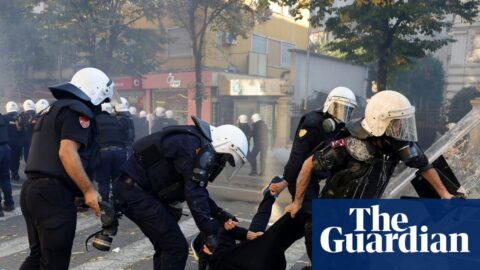 Riot police drag a hooded protester across a crosswalk during clashes in Tirana