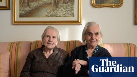Sisters Mariangela and Giovanna Marras, aged 99 and 101, sit together on a sofa