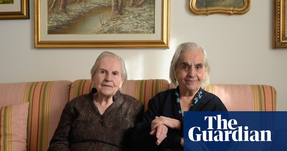 Sisters Mariangela and Giovanna Marras, aged 99 and 101, sit together on a sofa