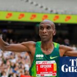 Eliud Kipchoge runs through the red finish tape with his hands in the air