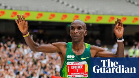 Eliud Kipchoge runs through the red finish tape with his hands in the air