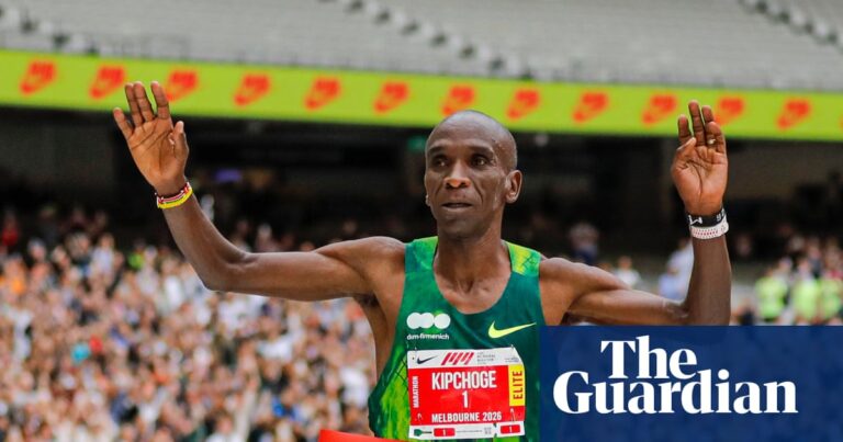 Eliud Kipchoge runs through the red finish tape with his hands in the air