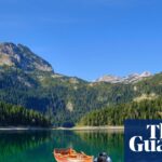 Kayaks and a rowing boat float beside a dock on Montenegro's Black Lake, mountains behind