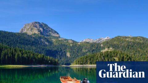 Kayaks and a rowing boat float beside a dock on Montenegro's Black Lake, mountains behind