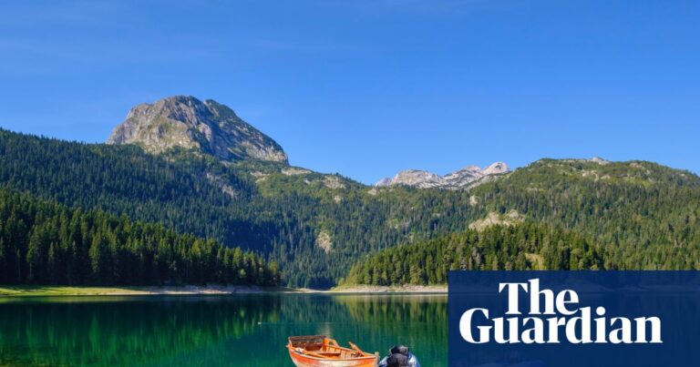 Kayaks and a rowing boat float beside a dock on Montenegro's Black Lake, mountains behind