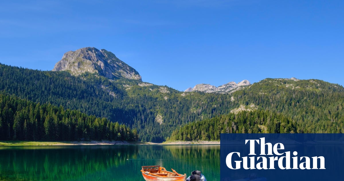 Kayaks and a rowing boat float beside a dock on Montenegro's Black Lake, mountains behind