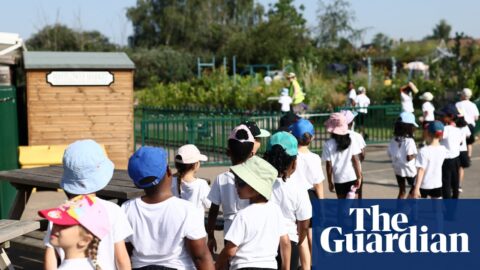 Pupils wearing hats and holding water bottles stand in a line outdoors