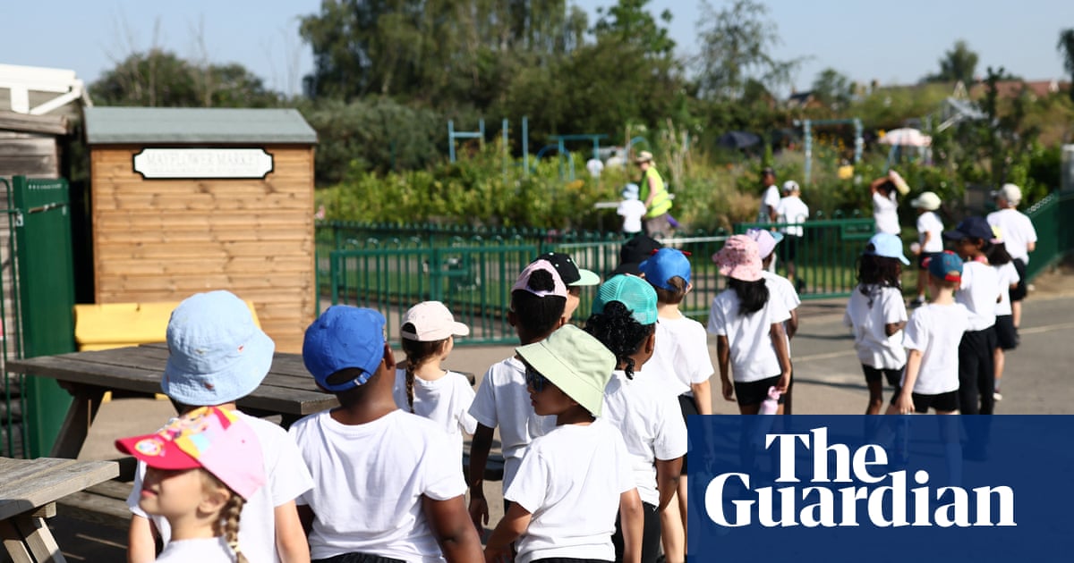 Pupils wearing hats and holding water bottles stand in a line outdoors