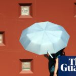Two people walk sharing a large pale blue umbrella during a heat warning in Los Angeles