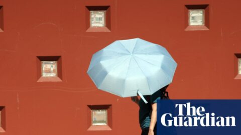 Two people walk sharing a large pale blue umbrella during a heat warning in Los Angeles