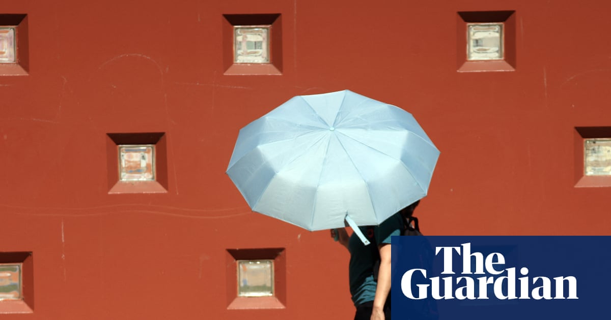 Two people walk sharing a large pale blue umbrella during a heat warning in Los Angeles