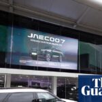 A white SUV is parked outside the Omoda/Jaecoo dealership, screen advertising "Jaecoo 7"