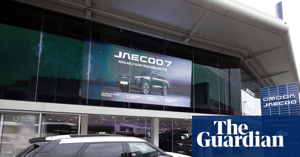 A white SUV is parked outside the Omoda/Jaecoo dealership, screen advertising "Jaecoo 7"